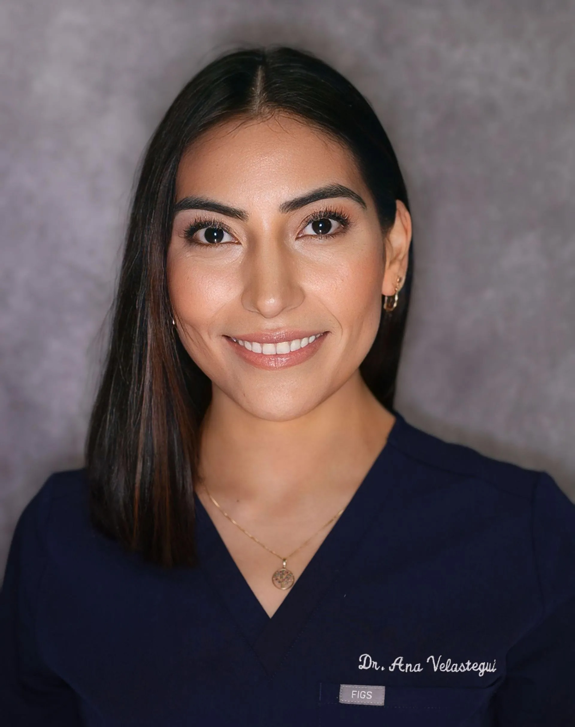 The image is a portrait of a woman wearing a white lab coat, smiling and looking directly at the camera.