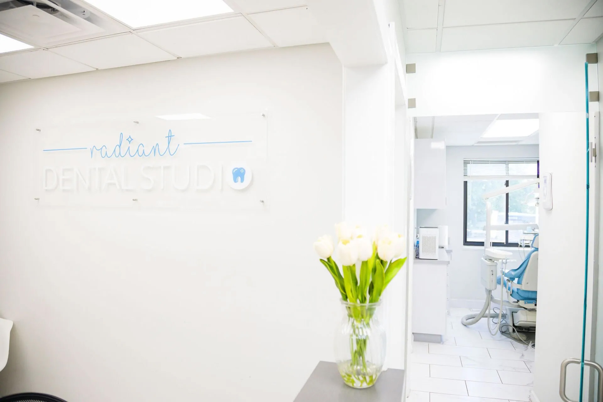 An interior view of a dental studio with a reception area, featuring a sign that reads  Radiant Dental Studio  and a white wall with a logo.