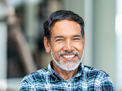 A smiling older man with a beard and mustache, wearing a plaid shirt, poses for the camera.