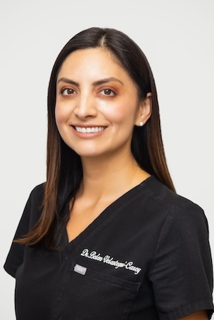 The image is a professional headshot of a woman wearing a white lab coat, smiling and posing for the camera.