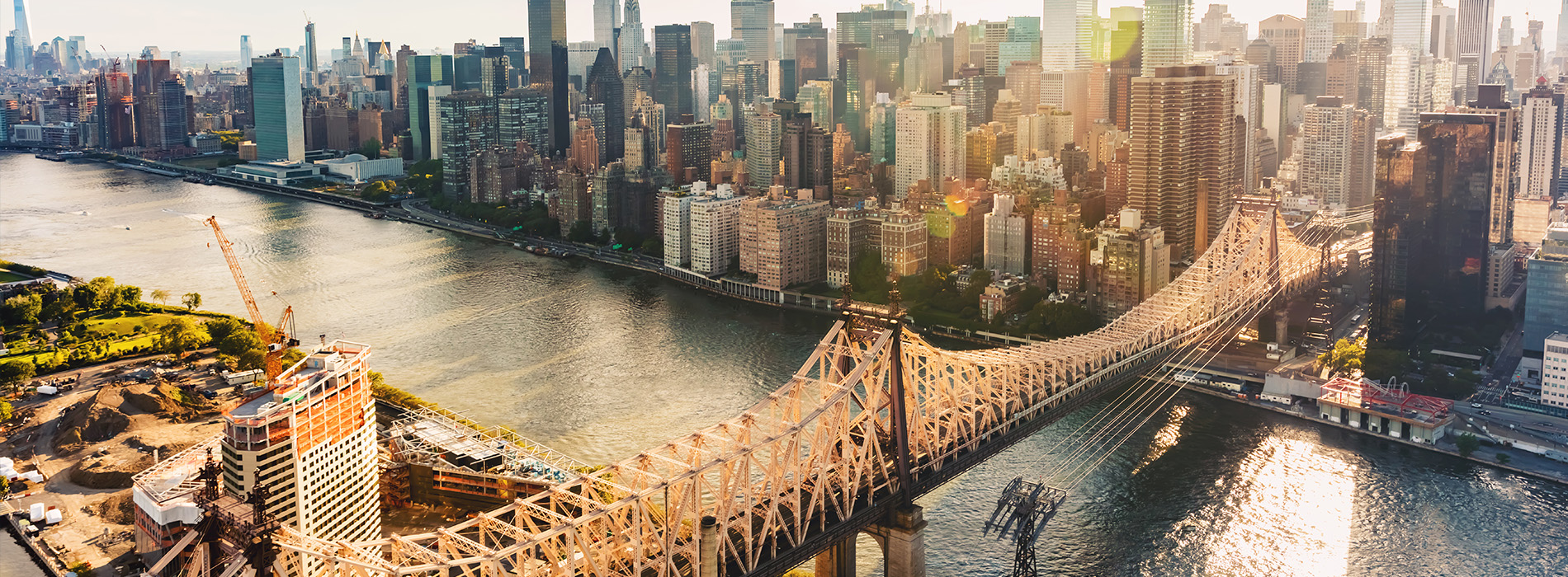 Aerial view of a bustling city skyline with the iconic Brooklyn Bridge and Manhattan skyscrapers, set against a clear blue sky.