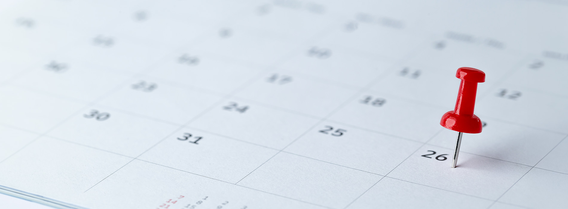 The image shows a calendar with the month of April visible, featuring a red push pin on top, set against a blurred background.