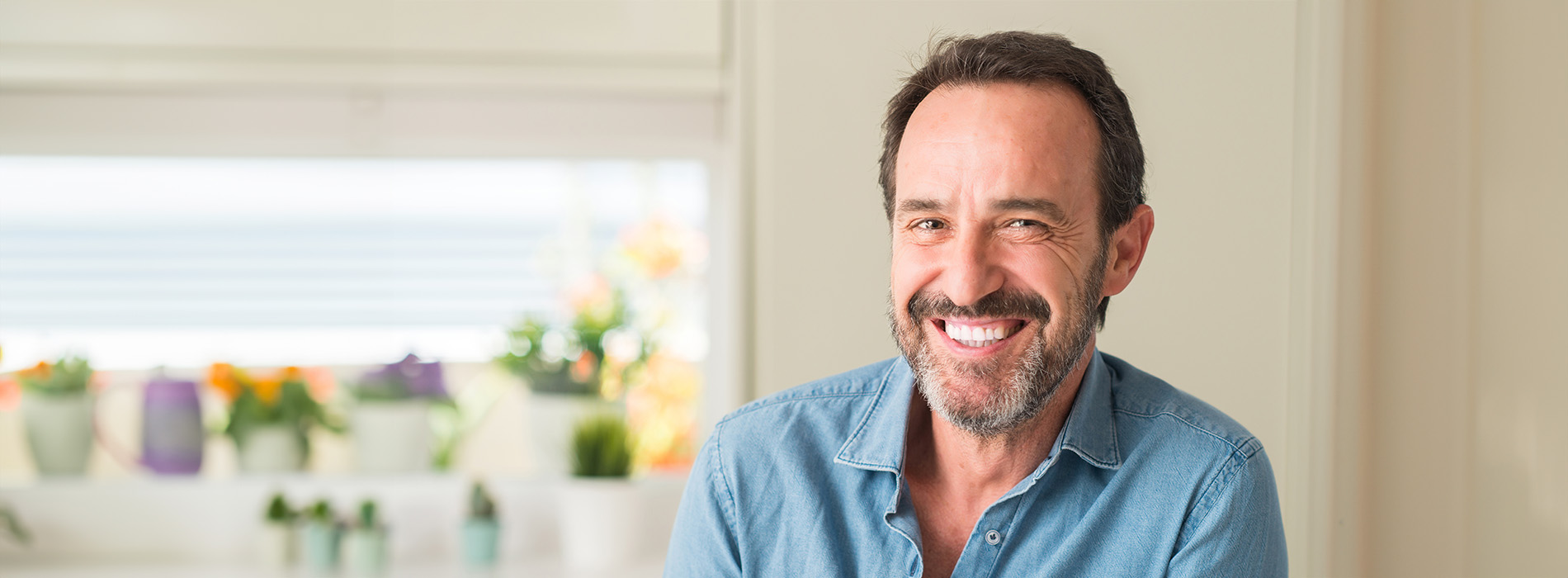 The image shows a man with a beard and mustache, smiling at the camera, wearing a casual blue shirt.