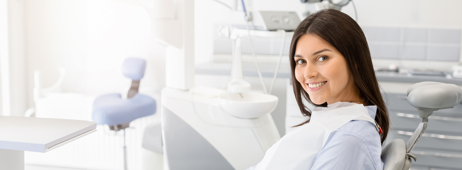 A dental office setting with a smiling woman in a blue uniform sitting at a desk.