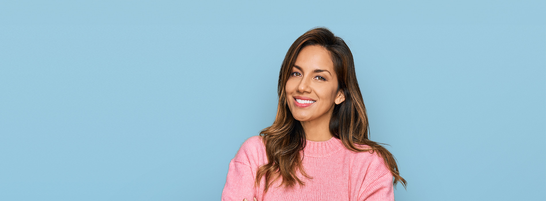 A woman with a smile, wearing a pink top, stands against a blue background.