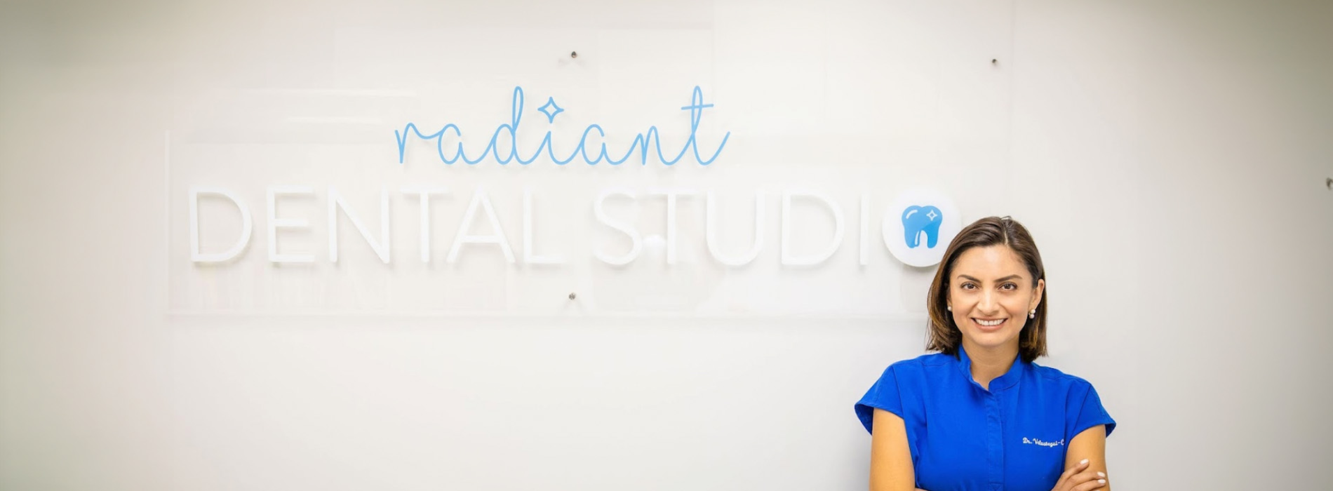 The image shows a person standing in front of a whiteboard with text that reads  RADIANT DENTAL STUDIO,  and the individual is smiling at the camera.