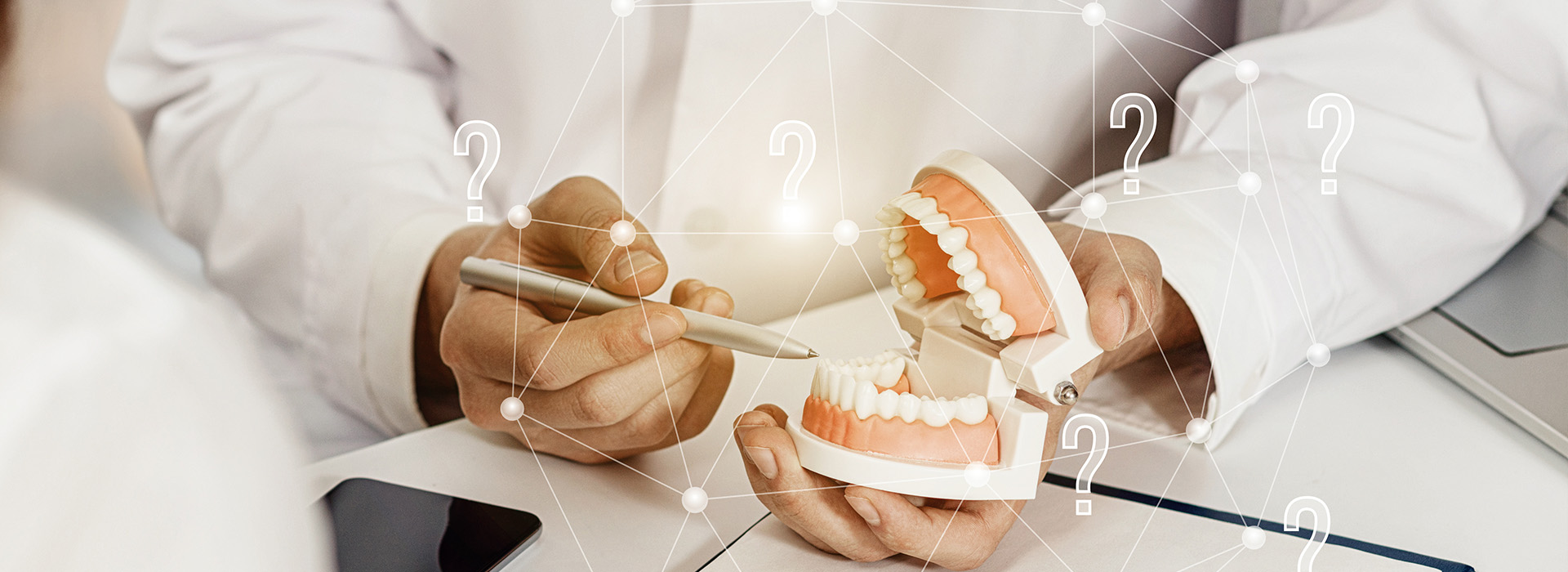 A person holding a tooth model with a digital interface displaying medical data in the background.