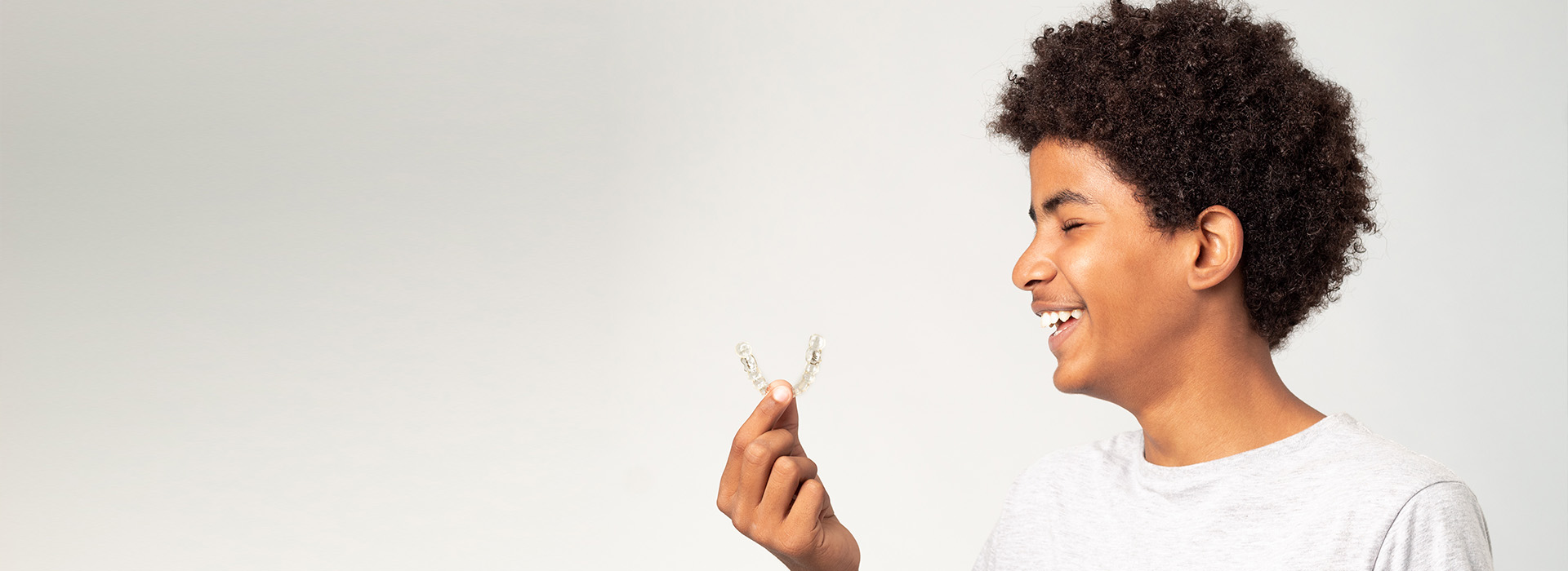 A young person holding a small plant, smiling at the camera against a neutral background.