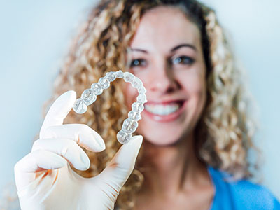 A smiling woman holding a clear tray with a transparent, elongated dental implant or bridge.