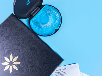 An open dental hygiene product box with a toothbrush and tube of toothpaste on a blue surface.