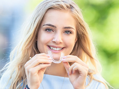 A young woman with blonde hair is smiling and holding a toothbrush with bristles.