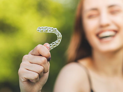 A smiling woman holding a transparent, tooth-shaped object in her hand.