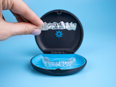 The image shows a person s hand holding an open dental impression tray with a blue background, revealing a transparent impression material inside.