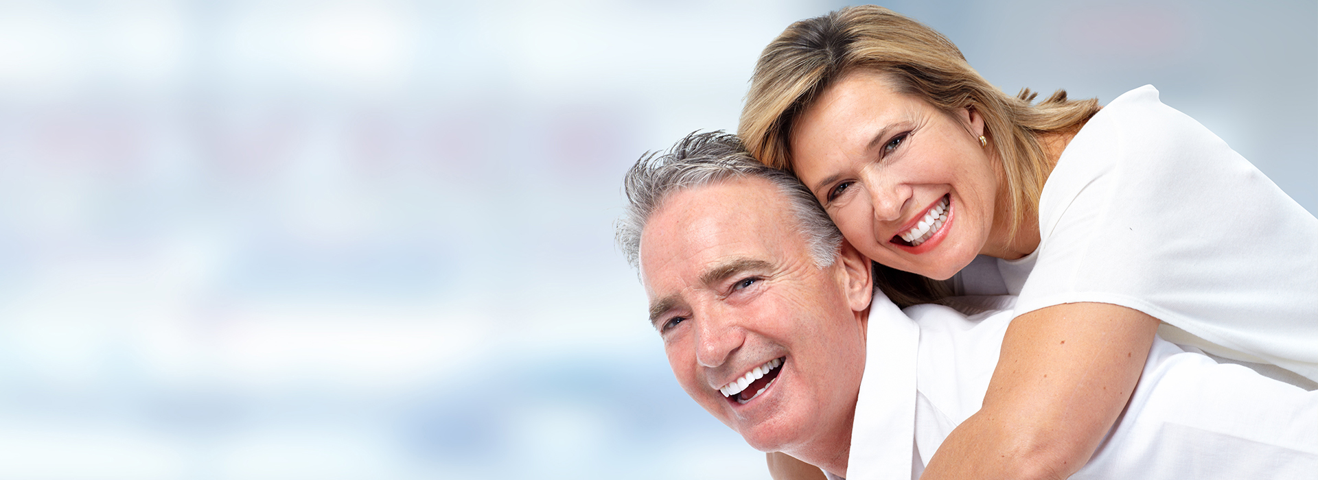 An elderly couple smiling and embracing in a close pose against a blurred background.