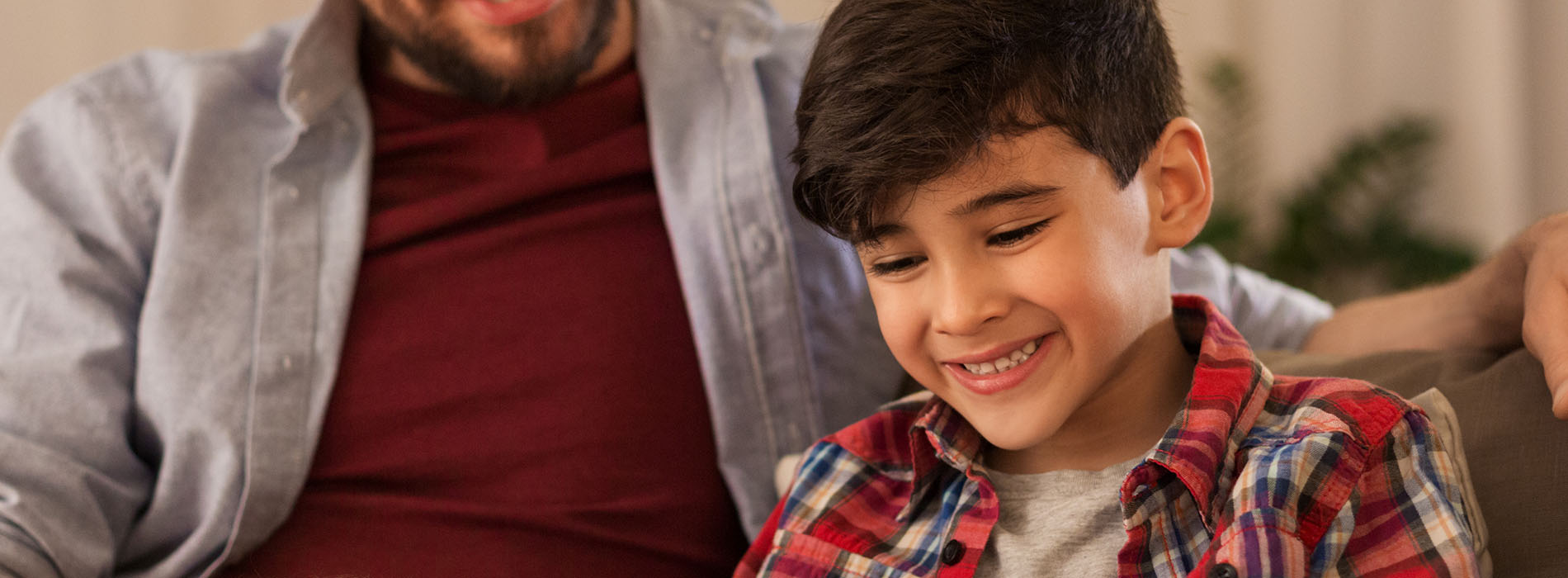 A man and a child are sitting on a couch, smiling at the camera.