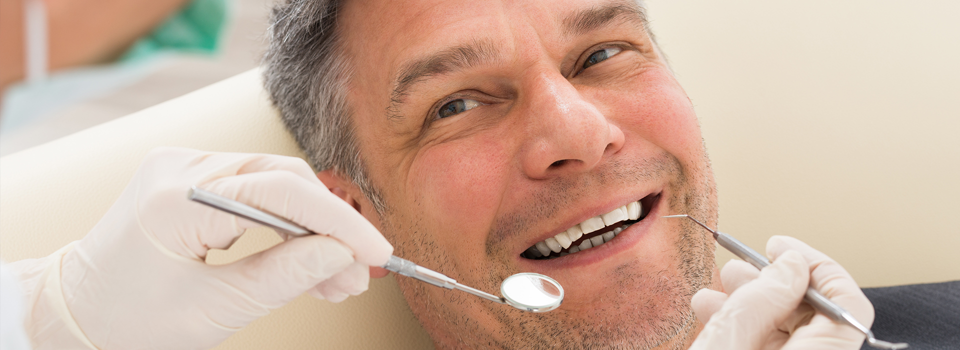 A man smiling while sitting in a dental chair, receiving dental care with dental tools visible around him.