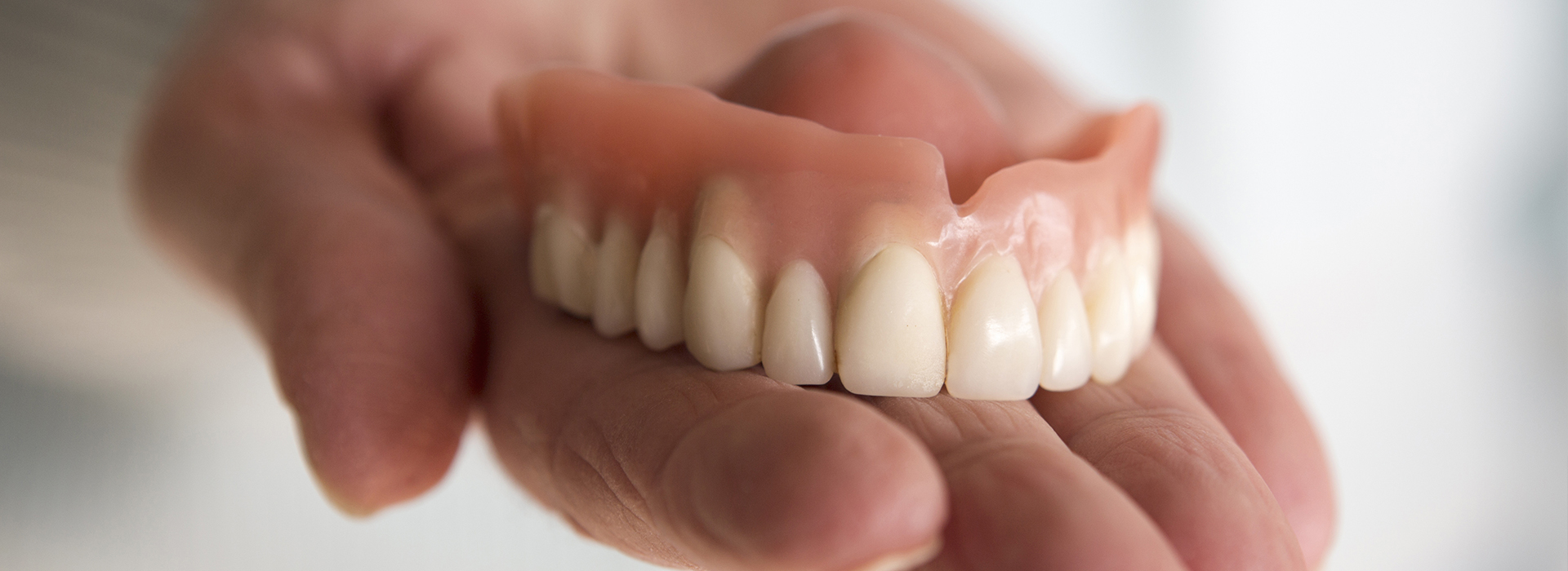 A person holding a set of dentures with a focus on the dental appliance.