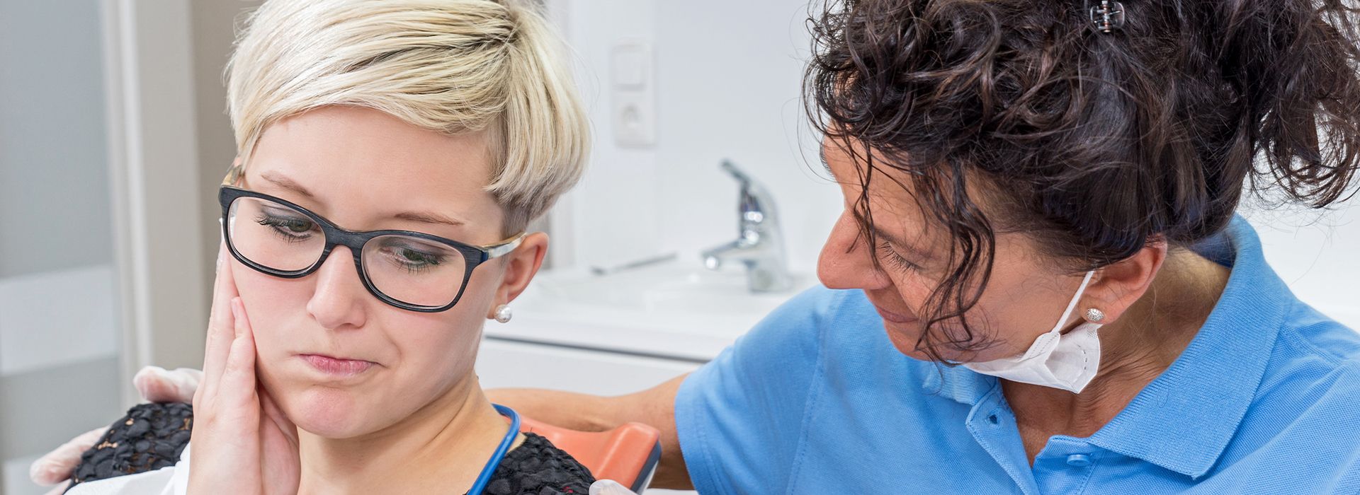 A split-screen photo showing a woman receiving dental care from a professional in the foreground, with a man in glasses observing or waiting for his turn in the background.