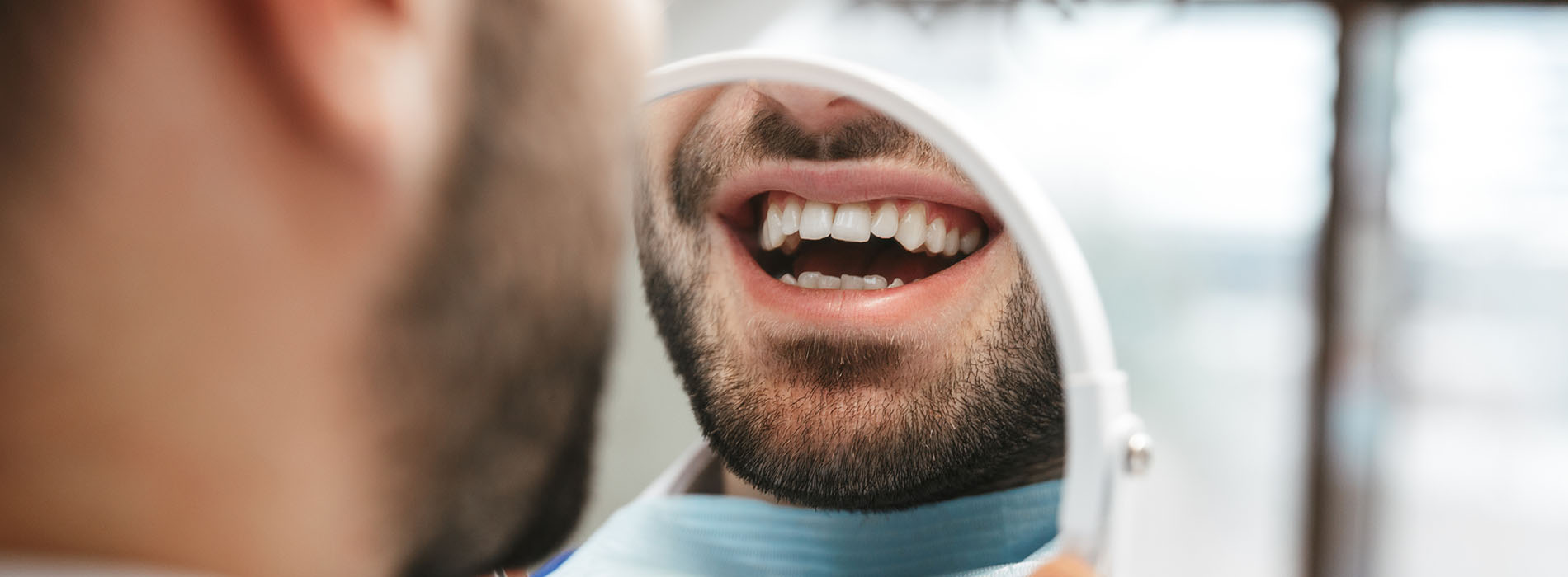 The image shows a man with his mouth open, displaying teeth, while another person appears to be examining or looking at him closely.