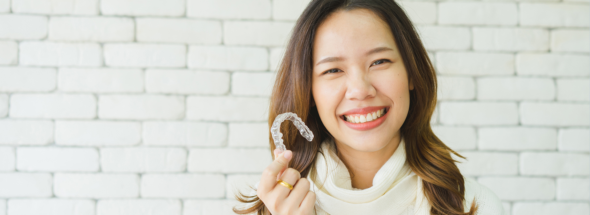 A smiling woman wearing a white top and holding a ring in her hand.