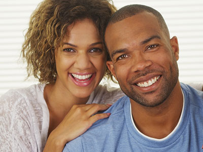 A man and a woman smiling at the camera, with the man wearing a blue shirt and the woman in a white blouse.