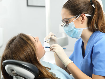 A dental hygienist is performing a teeth cleaning procedure on a seated patient.