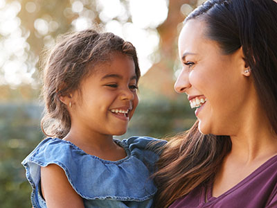 A woman and a child are smiling at the camera, with the child standing in front of the woman.