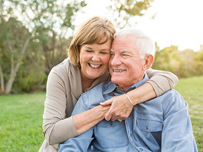 An elderly couple sharing a warm embrace outdoors.