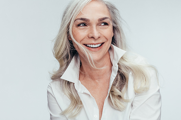 A woman with blonde hair and a radiant smile is the central figure in this image, which captures her from the chest up.