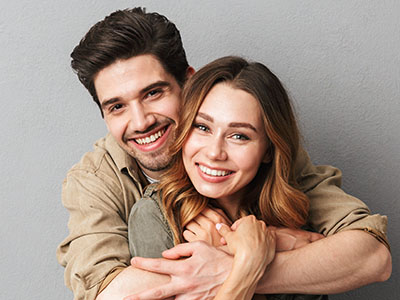 A man and a woman hugging closely, both smiling warmly at the camera.