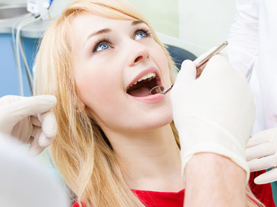 A woman in a dental chair receiving dental care, with a dentist performing the procedure and a dental hygienist assisting.