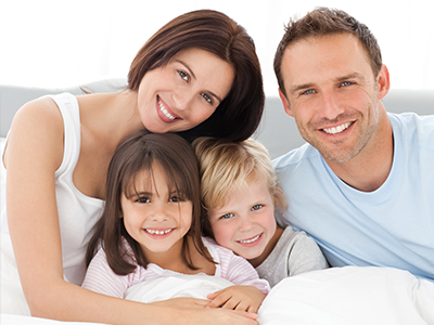 A family of four, including a man and woman with two children, posing for a photograph in bed.